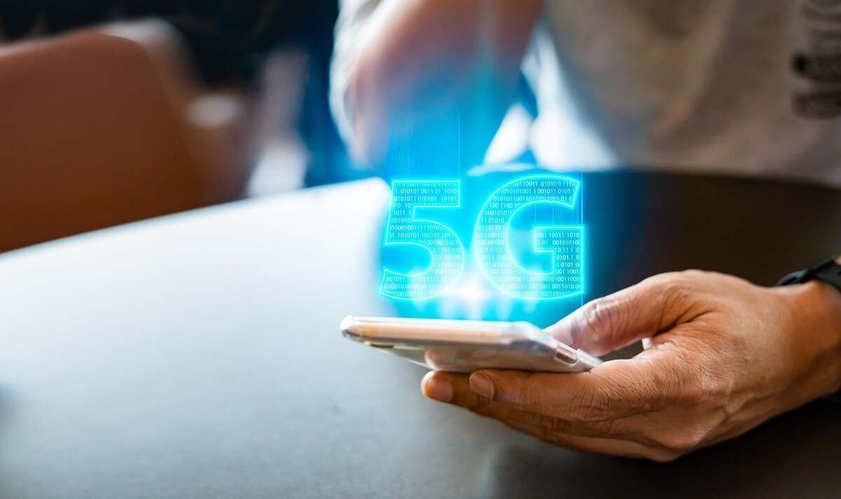 Femme tient un smartphone avec logo 5G en bleu, car elle est disponible à moins de 9€ sur le réseau d'Orange grâce à YouPrice